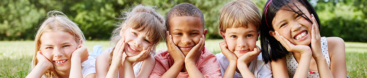 Five smiling students with their heads in their hands posing in the grass