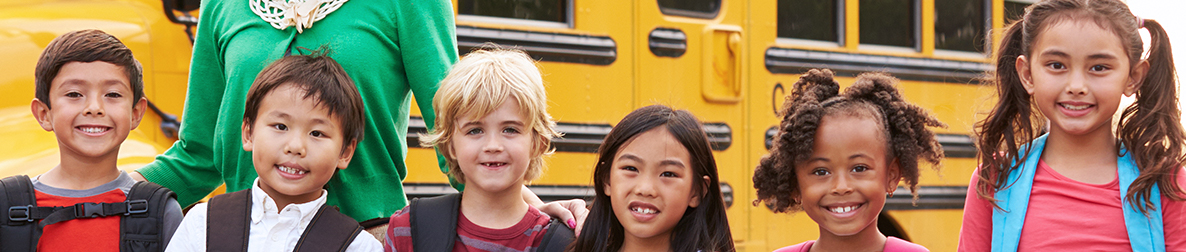 Six smiling students pose near a school bus